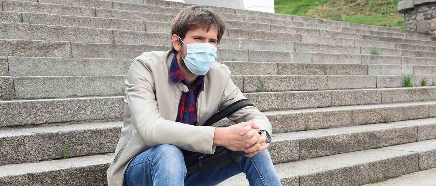 Ein Mann mit OP-Maske sitzt alleine im Freien auf einer breiten Treppe.